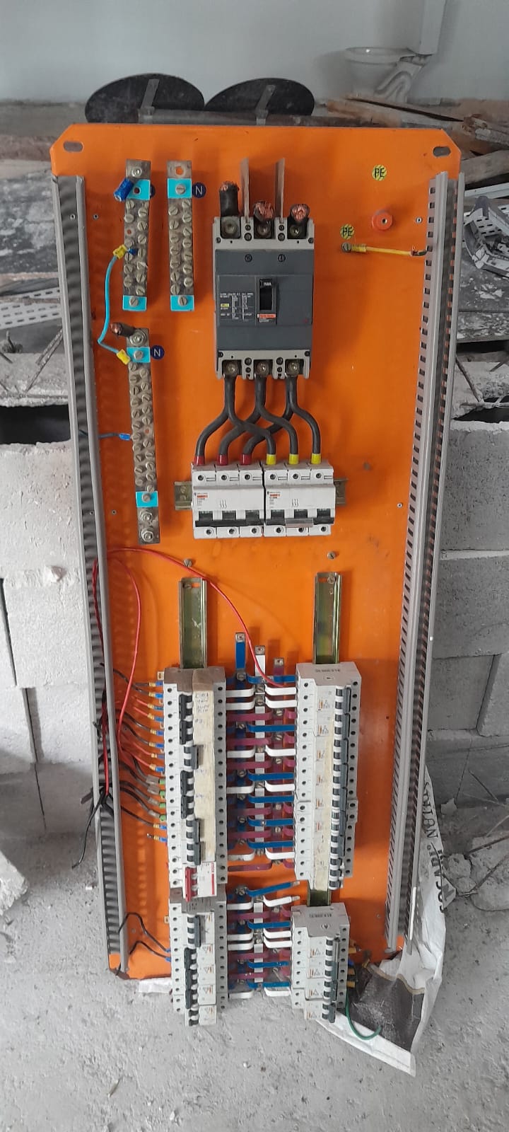 Painel laranja aberto em obra, com disjuntores e barramentos
